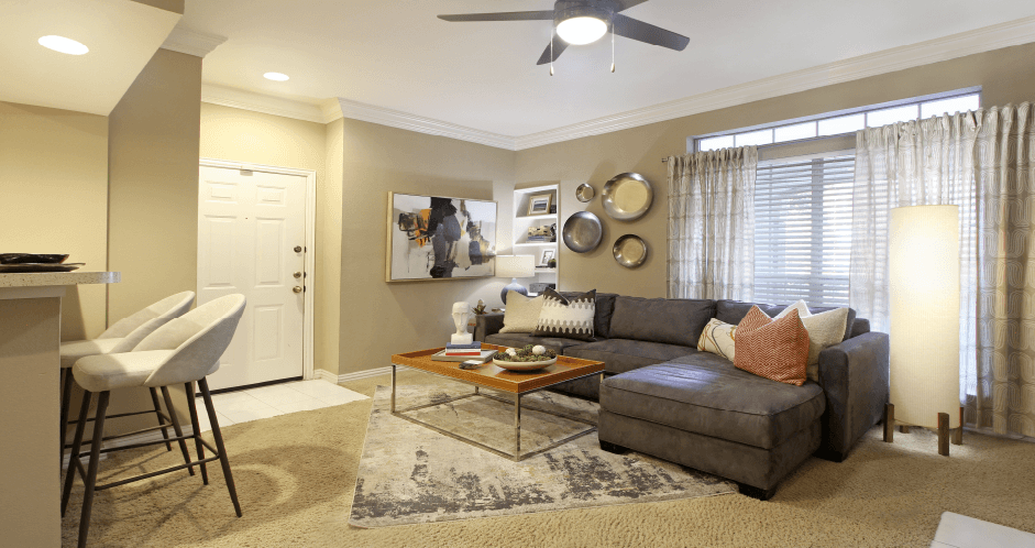Spacious living room with wood-burning fireplace with glass doors, ceiling fan, and 9-foot ceiling at Tuscany Lane Apartments in Houston.