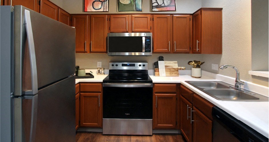 Luxury kitchen with wood plank floors, stainless steel appliances, honey brown cabinets, and white countertops at Lenox Village Apartments
