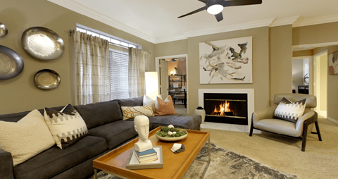 Spacious living room with wood-burning fireplace with glass doors, ceiling fan, and 9-foot ceiling at Tuscany Gate Apartments in Houston.