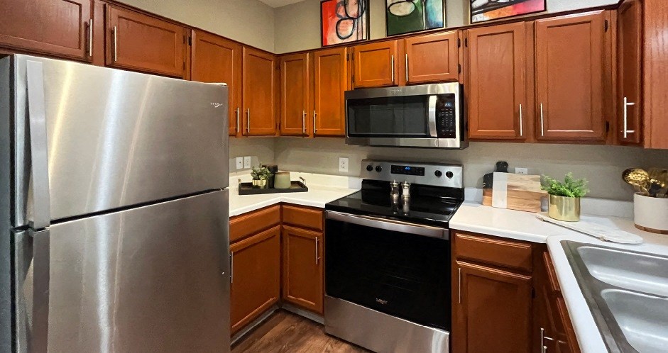 Luxury kitchen with wood plank floors, stainless steel appliances, honey brown cabinets, and white countertops at Lenox Village Apartments