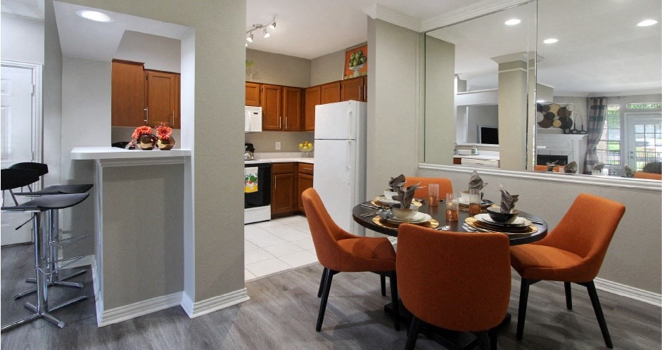 Luxury apartments with wood grain plank floors, dining room, u-shaped kitchen, mirror accent wall, and breakfast bar at Lenox Village Apartments in Lincoln, Nebraska