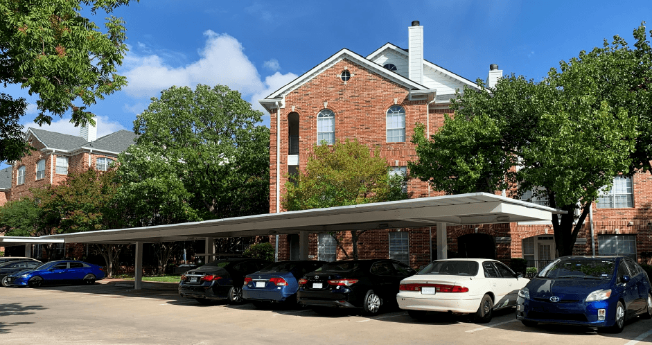 Gated luxury apartment community in north Dallas with red brick exteriors, covered parking, lots of trees, and beautiful landscaping at The Saxony Apartments
