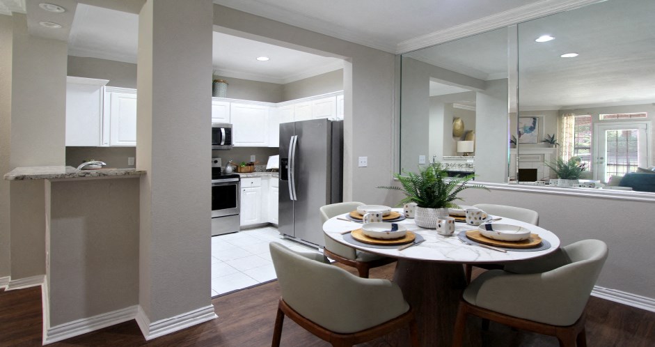 Spacious dining room, mirror accent wall, white cabinets, u-shaped kitchen, stainless steel appliances, wood plank floor and side-by-side refrigerator at TurtleCreek apartments in West Des Moines, Iowa