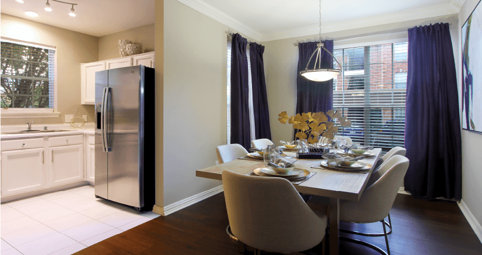 Spacious dining room with wood plank floors, oversized windows, kitchen with white cabinets, stainless-steel appliances, and side-by-side refrigerator at The Saxony Apartments