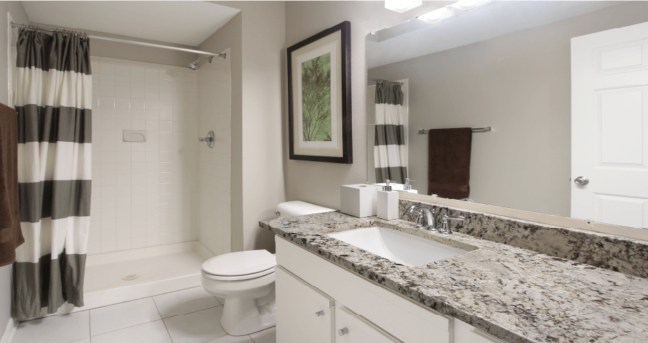 Spacious luxury bathroom with white cabinets, granite countertops, gray wall color, porcelain tile floor, and walk-in shower at Breckenridge Apartments