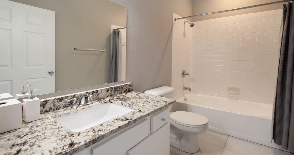 Spacious luxury bathroom with white cabinets, granite countertops, gray wall color, porcelain tile floor, soaking tub and tiled shower at Breckenridge Apartments in Omaha, Nebraska