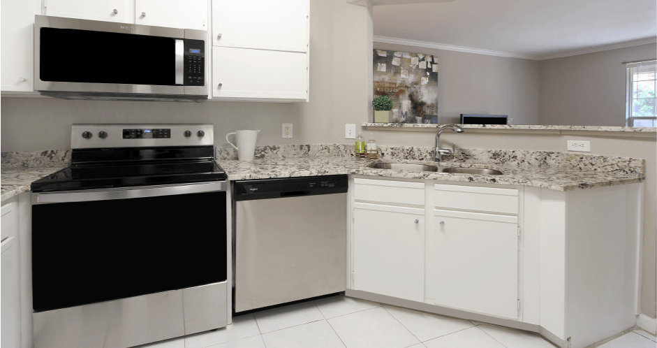 Spacious kitchen with white cabinets, granite countertops, stainless steel appliances, serving bars, and porcelain tile floors at Breckenridge Apartments in southwest Omaha, Nebraska