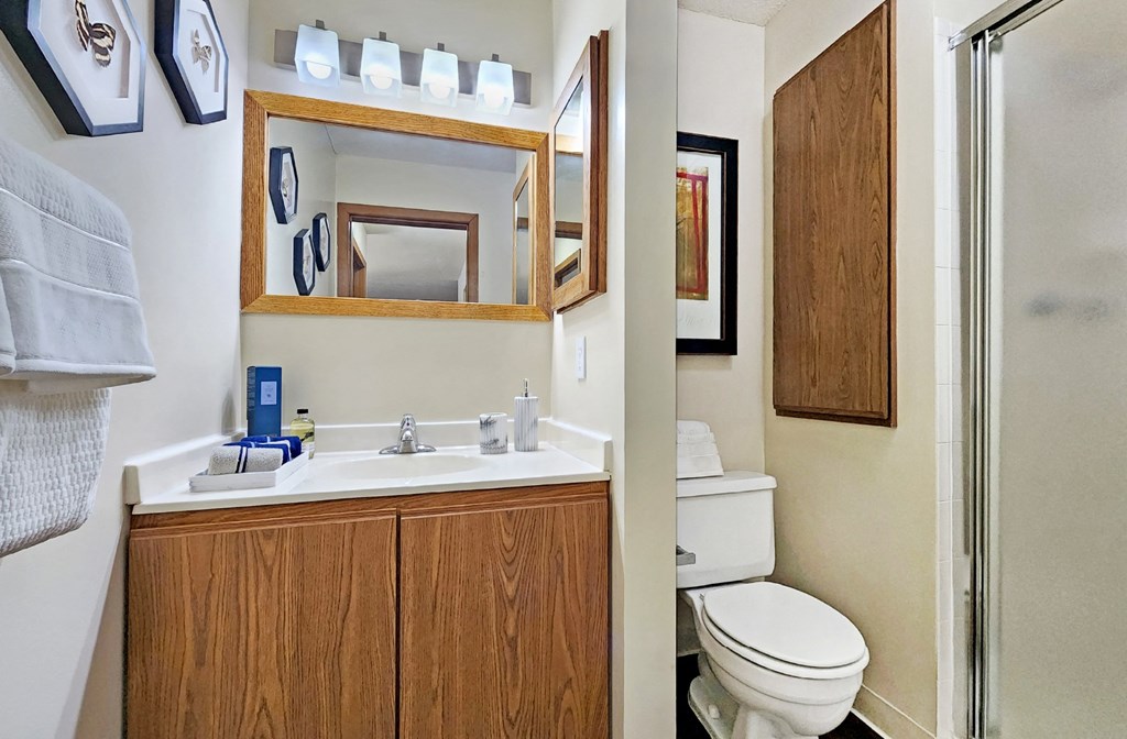 Spacious bathroom with glass shower, honey brown toned cabinets, and white countertops at Claremont Apartments in Minnetonka Minnesota.