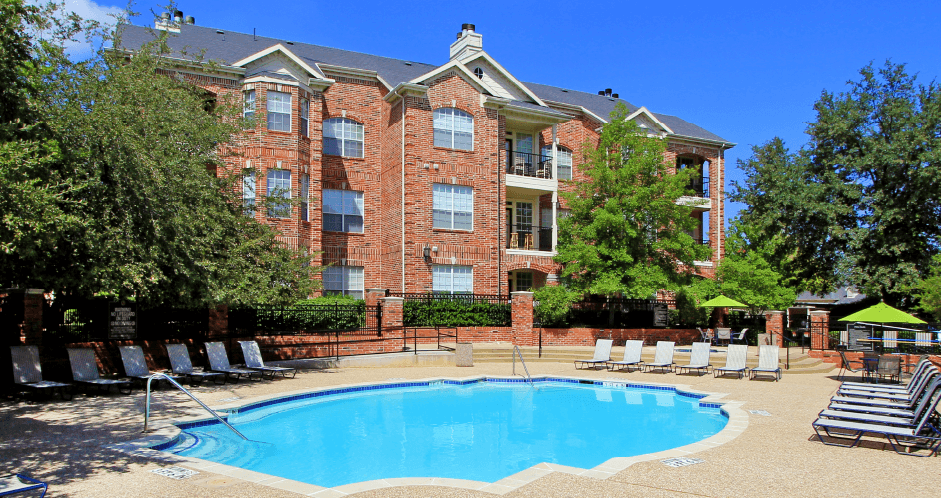 Gated apartment community with brick exteriors, lush landscaping, two swimming pools with poolside lounge chairs, spa, and sauna at The Saxony Apartments