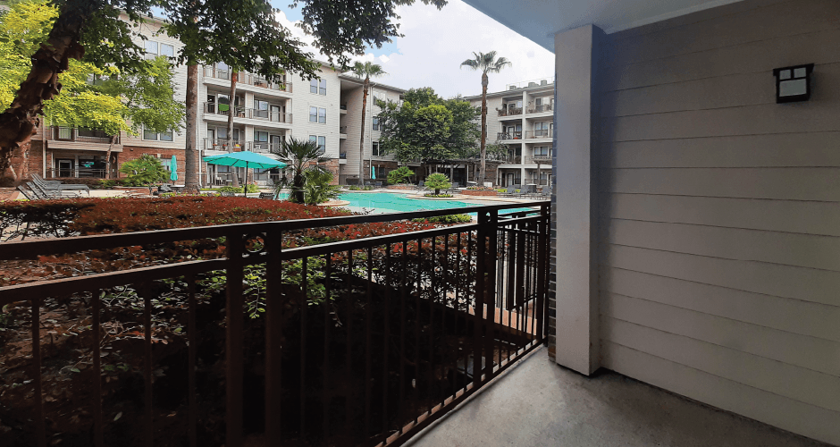 Luxury apartments with spacious balconies, resort-style pool with fountains, pool-side lounge chairs, spa, and palm trees at The Voss Apartments in Houston.