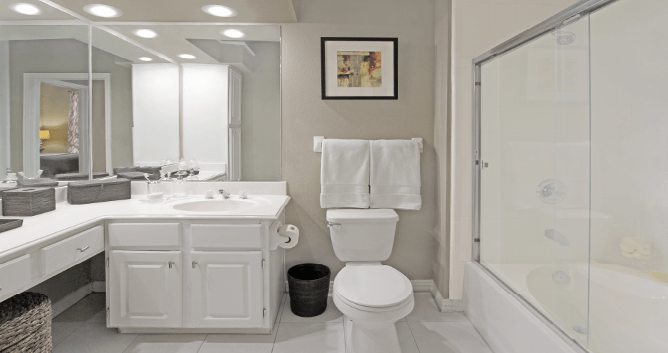 Spacious luxury bathroom with built-in cultured marble vanity, roman tub with glass shower, and porcelain tiled floor at The Biltmore Apartments in Omaha, Nebraska