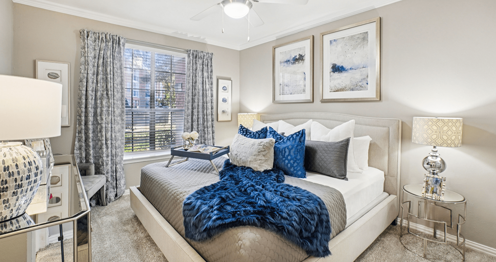 A bedroom with a bed covered in a blue blanket and two lamps on either side of the bed.