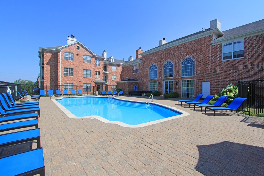 an outdoor pool with blue chairs and a brick building