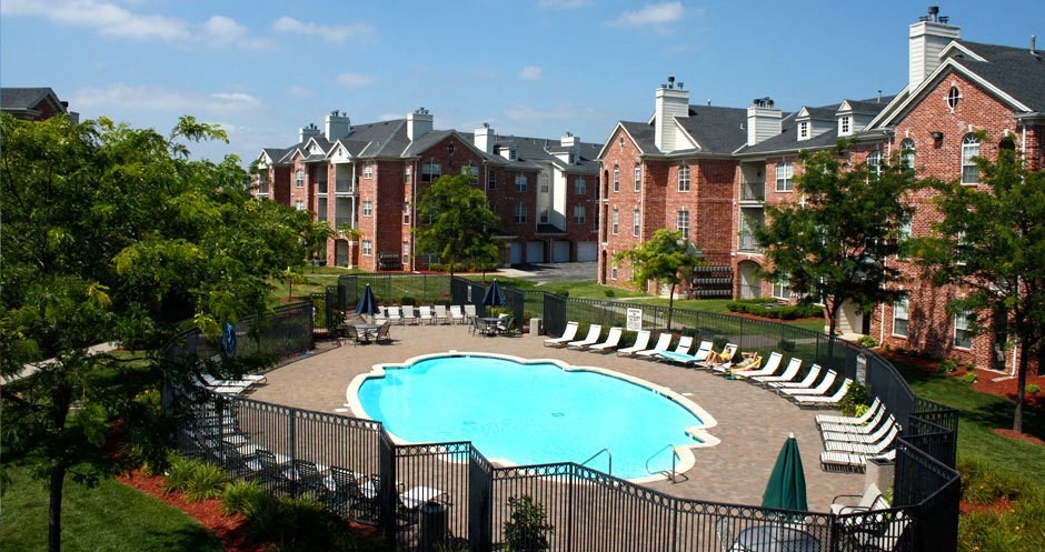 an outdoor pool with lounge chairs and umbrellas in front of a brick building