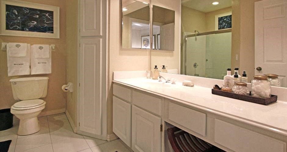 Luxury apartments with white cabinets, linen closet, extra cabinet space, cultured marble vanity, built-in vanity, roman tub with glass door and shower, and porcelain tiled floor at The Biltmore Apartments in Omaha, Nebraska