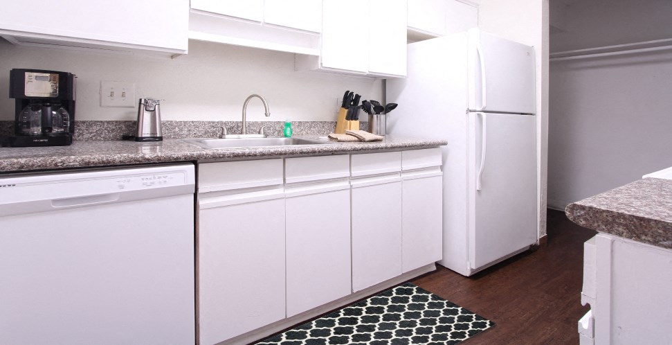Bright white kitchen with granite countertops and hardwood floors at at Briarwood Apartments in Houston.