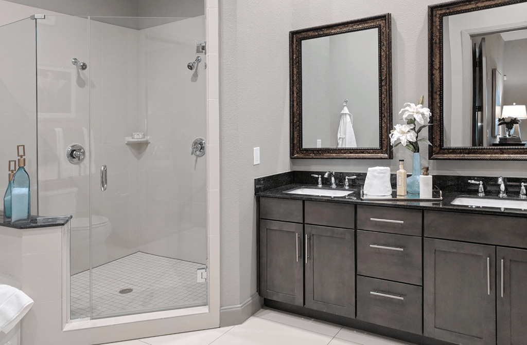 Luxury bath suite with double sink granite slab vanity top, frameless glass walk-in shower with separate soaking tub at Le Palais Apartments in Houston.