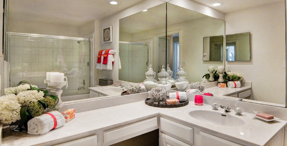 Spacious bathroom with oval soaking tub with glass enclosure, cultured marble vanity, glass shower, and built-in vanity at Tuscany Apartments in Houston.