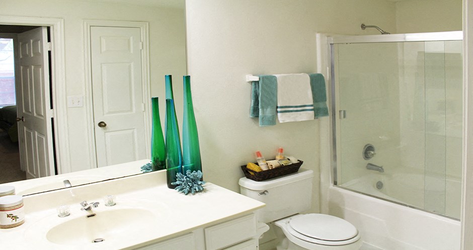 Spacious bathroom with oval soaking tub with glass enclosure, cultured marble vanity, and glass shower at Tuscany Apartments in Houston.