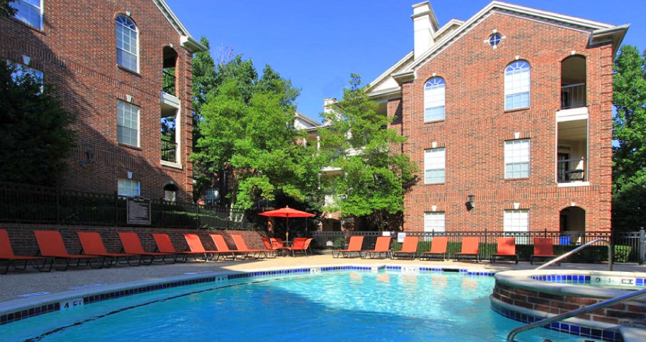 Gated community near the Galleria with brick exteriors, lush landscaping, two swimming pools with poolside lounge chairs, spa, and sauna at The Dorchester Apartments in Houston.