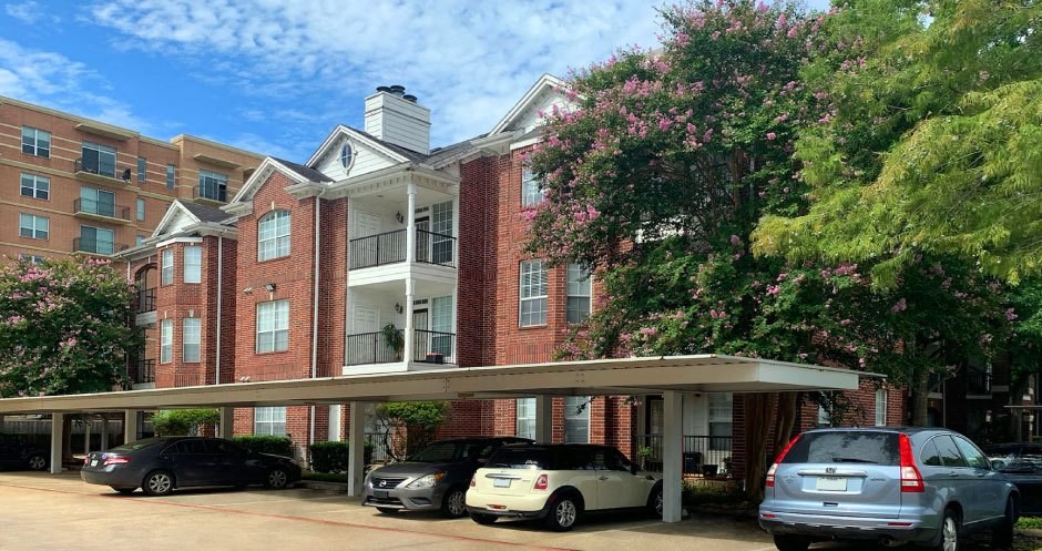 Luxury apartments in a gated community with covered car ports and red brick exteriors at Tuscany Oaks Apartments in Houston.