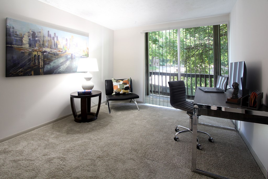 A living room with a grey carpet and a painting on the wall.