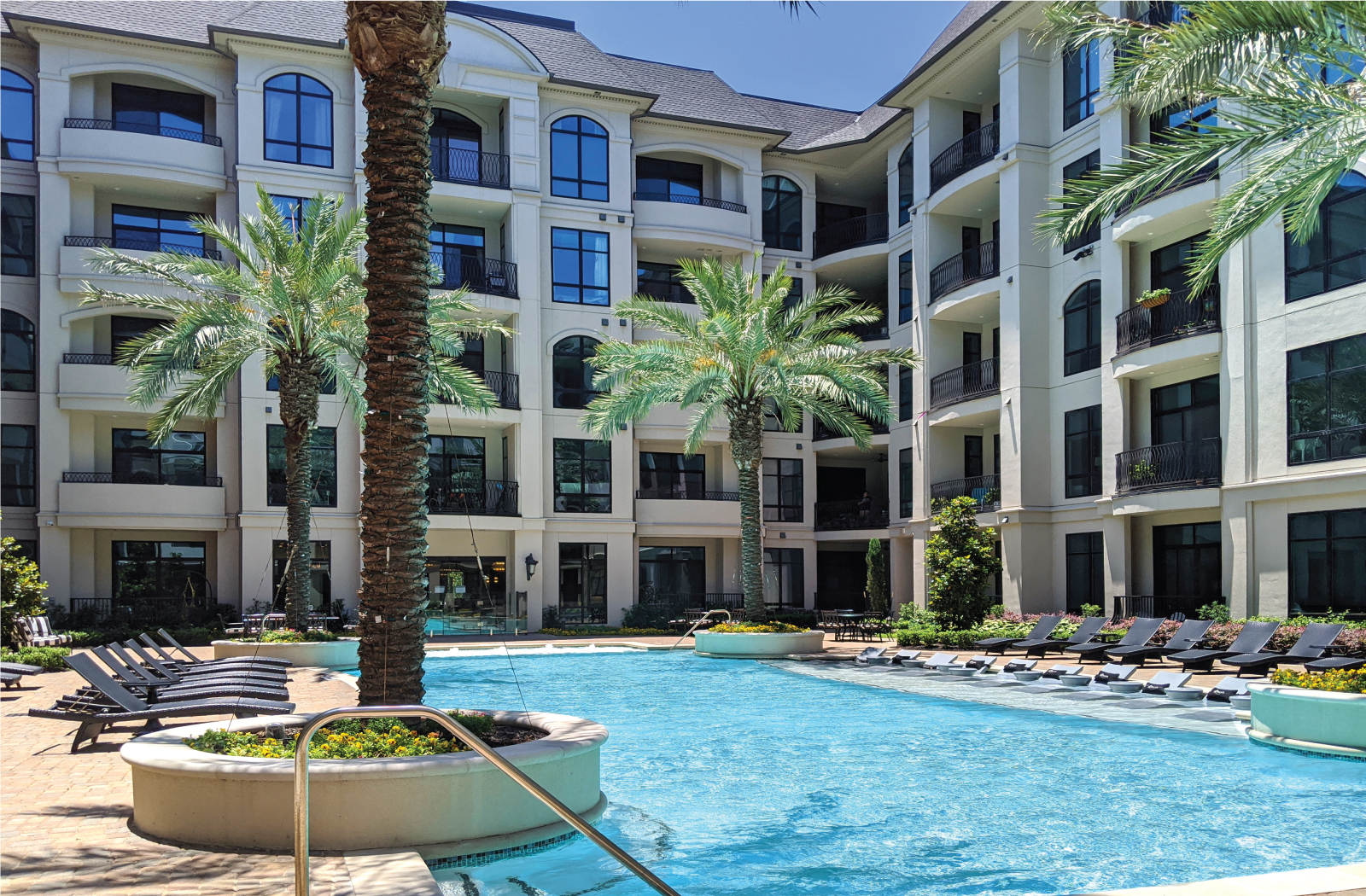 Luxury apartments with resort-style pool with palm trees, Baja shelf, fountains, lap lane, outdoor lounges, and grilling station at Le Palais Apartments in Houston.