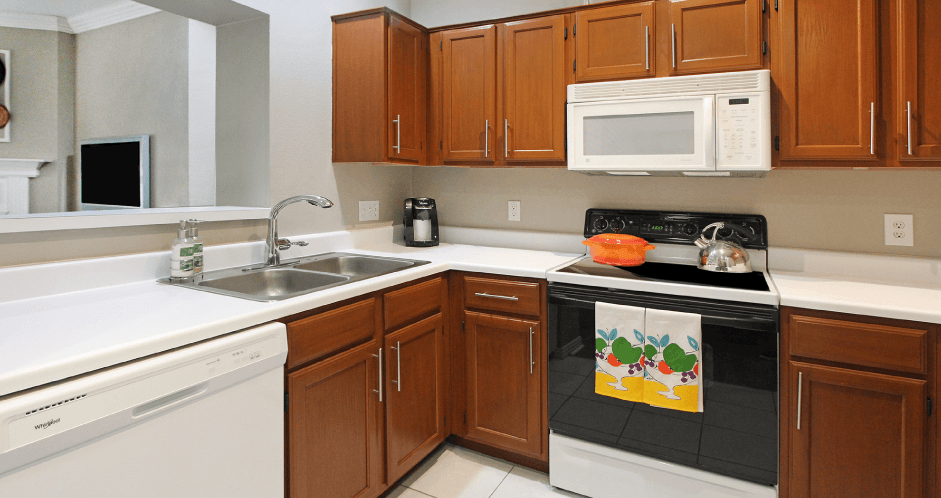 Luxury apartments with honey brown cabinets, tiled floors, white countertops, and u-shaped kitchen at Lenox Village Apartments in Lincoln, Nebraska