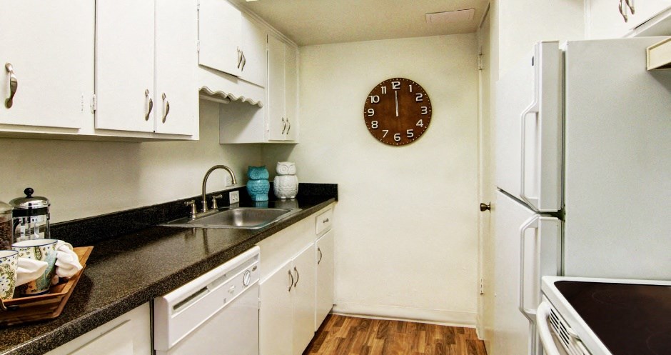 Apartments near the Galleria with bright white kitchens, black countertops, and wood plank flooring at Plantation apartments in Houston.