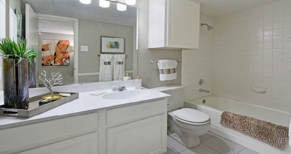Spacious bathroom with white cabinets and white porcelain tile at Preston Village Apartments in North Dallas