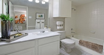 Spacious bathroom with white cabinets and white porcelain tile at Preston Village Apartments in North Dallas - Photo Gallery 15