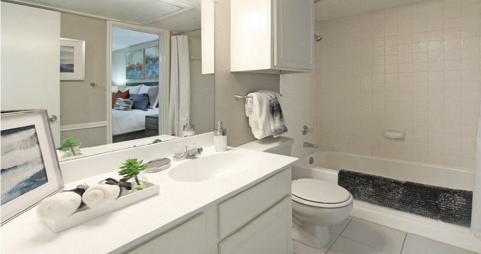 Spacious bathroom with white cabinets and white porcelain tile at Preston Village Apartments in North Dallas