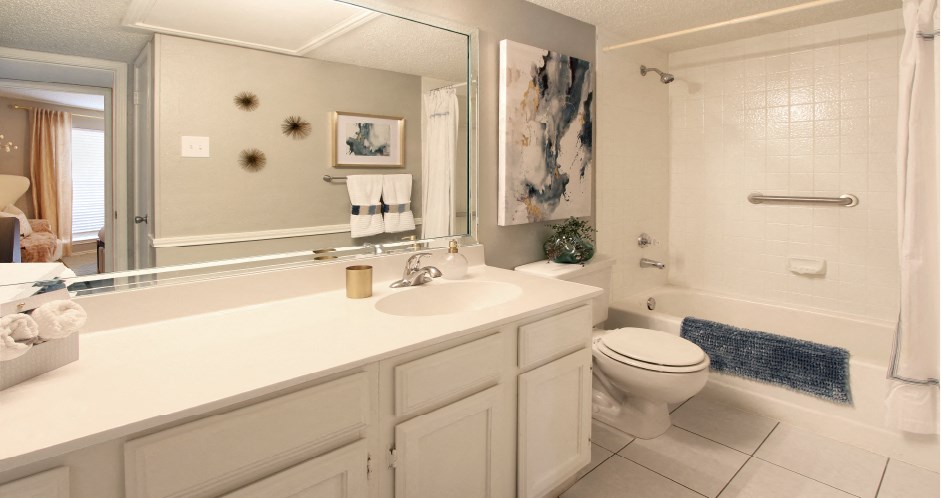 Spacious bathroom with white cabinets and white porcelain tile at Preston Village Apartments in North Dallas