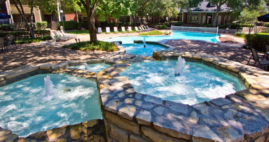 Luxury apartments with beautiful fountains, beautiful landscaping, swimming pool with poolside lounge chairs, and scenic views at Preston Village Apartments in north Dallas