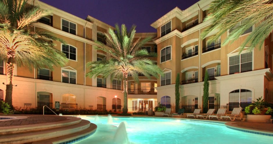 a large swimming pool in front of a hotel with palm trees