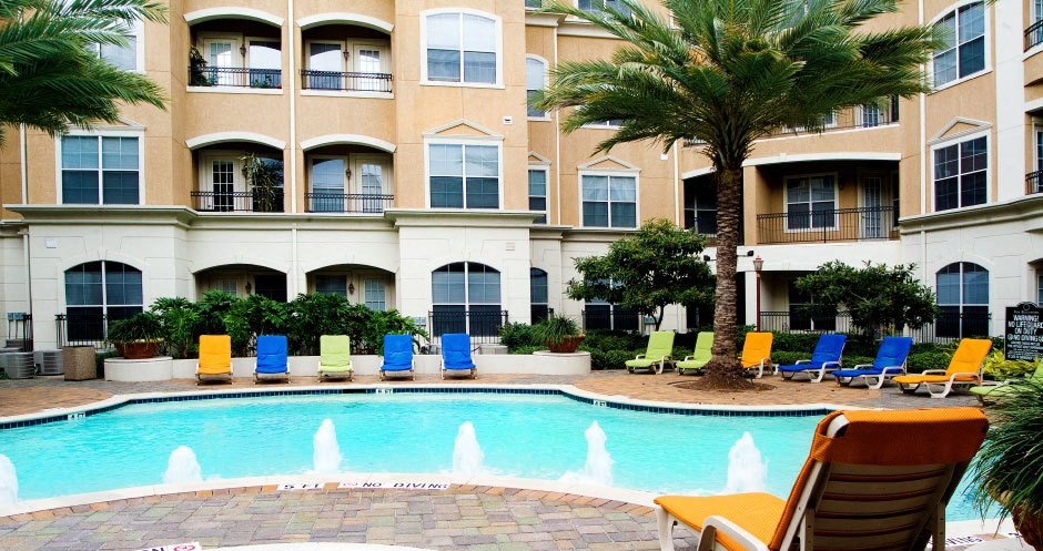 a large swimming pool with chairs and a building in the background