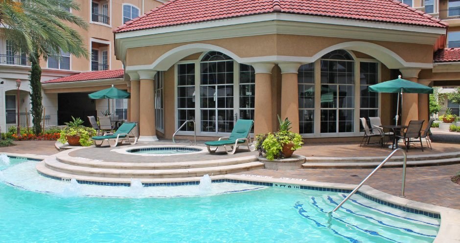 Luxury apartments with resort-style pool with fountains, pool-side lounge chairs, spa, and palm trees at Tuscany Court Apartments in Houston.