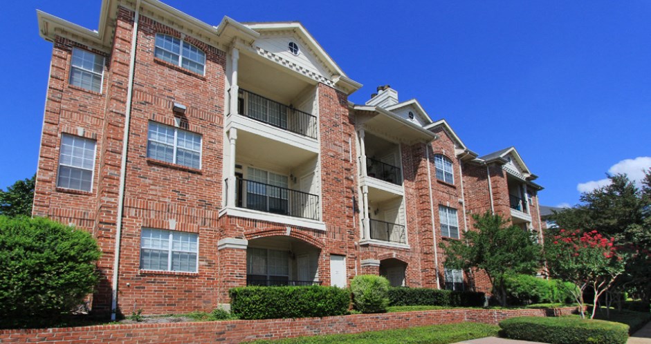 Gated luxury apartment community in north Dallas with red brick exteriors, large patio, and beautiful landscaping at The Saxony Apartments