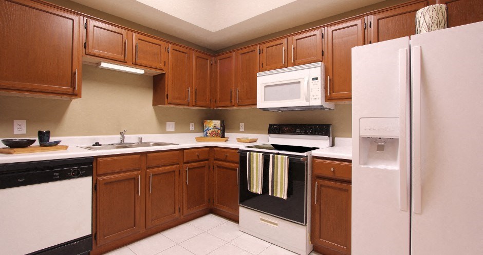 Spacious dining room and kitchen with honey brown toned cabinets with modern silver hardware, and white appliances.