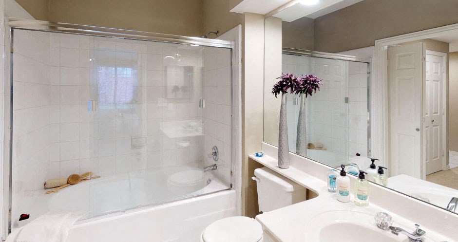 Luxury bathroom with white cabinets, cultured marble vanity, oval soaking tub, and glass shower at The Saxony Apartments