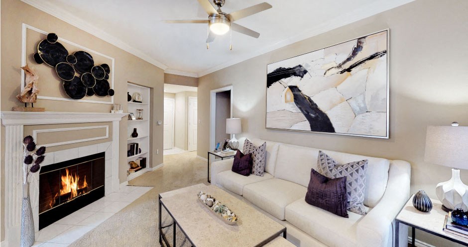 Spacious living room with wood-burning fireplace with glass doors, ceiling fan, crown molding, and built-in bookshelves at Tuscany Gate Apartments in Houston.