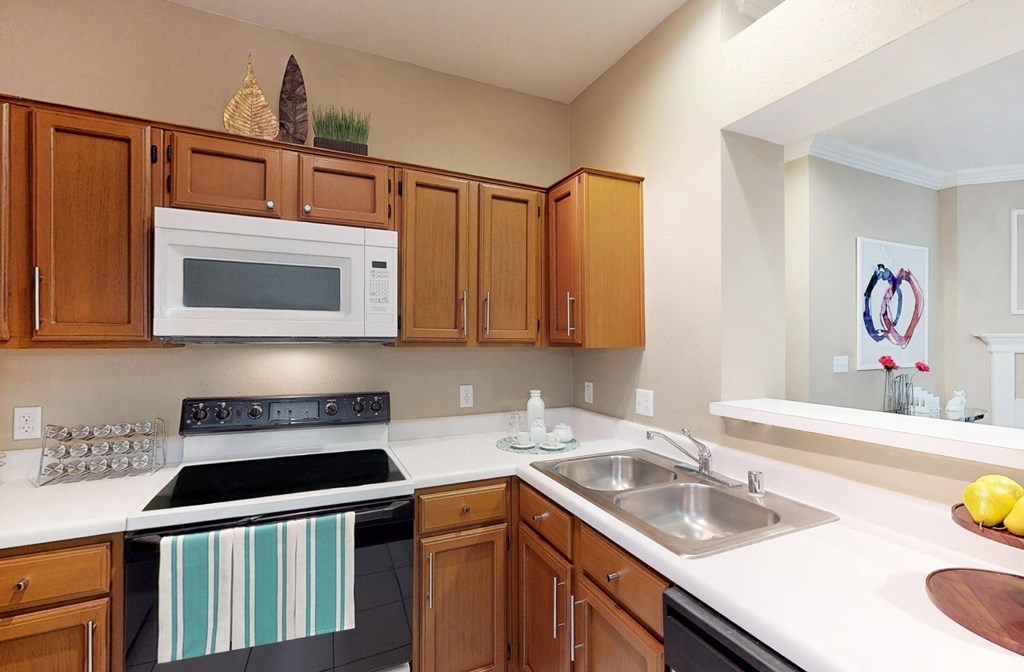 Spacious kitchen with honey brown toned cabinets, u-shaped kitchen, tile floors, and lots of counter space at Tuscany Park Apartments in Houston