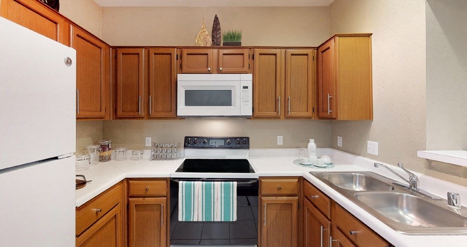Spacious kitchen with honey brown toned cabinets, u-shaped kitchen, tile floors, and lots of counter space at Tuscany Park Apartments in Houston