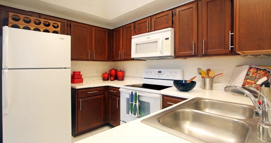 Spacious kitchen with honey brown toned cabinets, lots of counter space, white appliances, tile floor and recessed ceiling at Tuscany Oaks Apartments in Houston