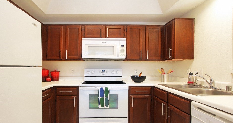 Spacious kitchen with honey brown toned cabinets, lots of counter space, white appliances, tile floor and recessed ceiling at Tuscany Oaks Apartments in Houston