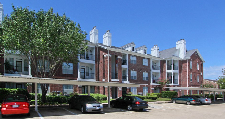 Luxury apartments in a gated community with covered carports and red brick exteriors at Tuscany Oaks Apartments in Houston.