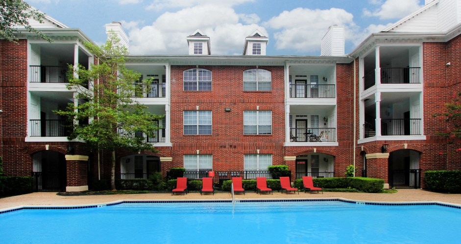 Luxury swimming pool with spacious sundeck, beautiful landscaping, and poolside lounge seating at Tuscany Oaks Apartments in Houston.