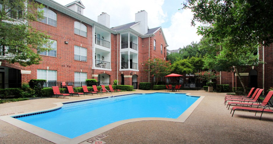 Luxury swimming pool with spacious sundeck, beautiful landscaping, and poolside lounge seating at Tuscany Oaks Apartments in Houston.