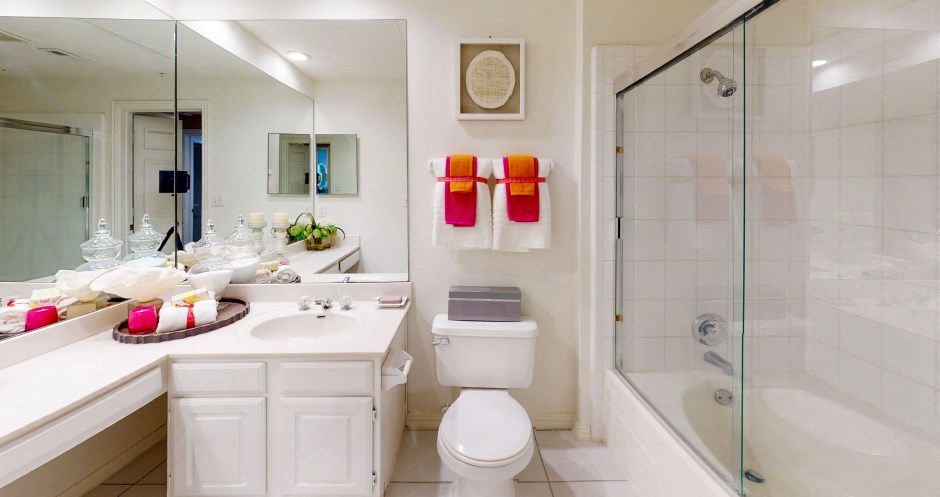 Spacious bathroom with oval soaking tub with glass enclosure, cultured marble vanity, glass shower, and built-in vanity at Tuscany Apartments in Houston.