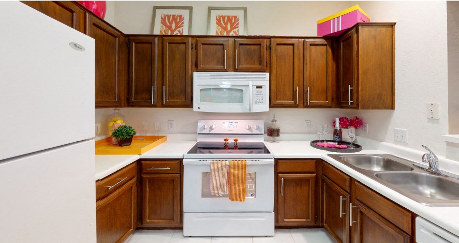 Spacious kitchen with honey brown toned cabinets with modern silver hardware, and white appliances.